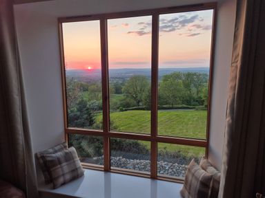 A window seat with cushions overlooking trees and fields at sunset at Newlands Barn in Wellington