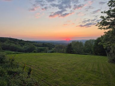 A grassy field with trees and a sunset in the distance at Newlands Barn in Wellington