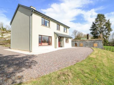 A two-story house with a gravel driveway and green grass lawn at Teach Ards Kilgarvan County Kerry