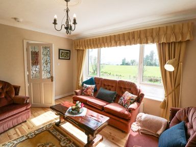 A sitting room with sofa chairs a wooden coffee table and large window with curtains at Teach Ards in Kilgarvan County Kerry