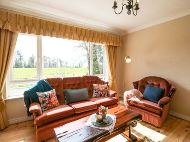 A living room with two brown sofas a wooden coffee table and large windows with curtains at Teach Ards in Kilgarvan County Kerry