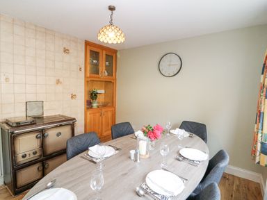 A dining room with an oval table set for six people a wall clock a wooden cabinet and an old stove at Teach Ards Kilgarvan County Kerry
