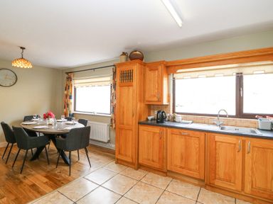 A kitchen with wooden cabinets a black countertop a sink and a dining area with a round table and six chairs at Teach Ards in Kilgarvan County Kerry