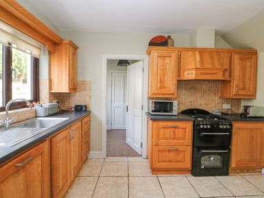 A kitchen with wooden cabinets a black oven a microwave a toaster and a sink at Teach Ards in Kilgarvan County Kerry