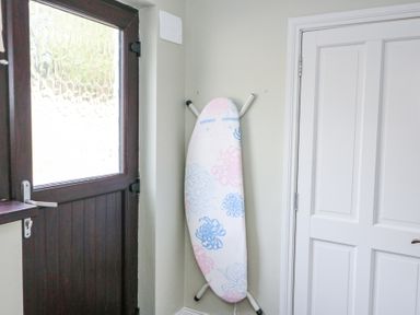 An ironing board with a floral cover standing against a wall next to a white door and a wooden door with textured glass at Teach Ards in Kilgarvan County Kerry