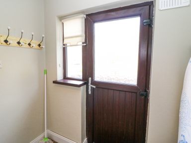 A wooden door with a window and a small window beside it a mop leaning against the wall and wall hooks in a utility room at Teach Ards Kilgarvan County Kerry