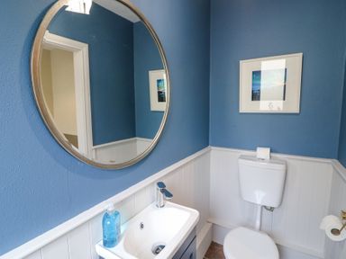 A bathroom with a round mirror above a sink and a toilet with blue walls and white wainscoting at Teach Ards in Kilgarvan County Kerry