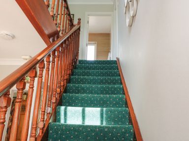 A staircase with green carpet and wooden banister leading to a hallway at Teach Ards in Kilgarvan County Kerry