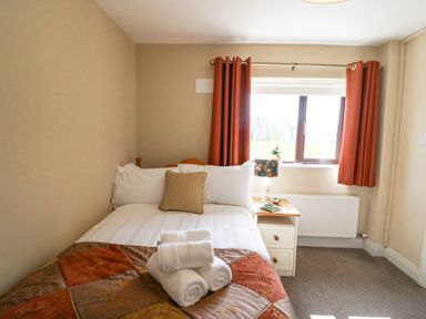 A bedroom with a bed pillow bedside table lamp and window with red curtains at Teach Ards Kilgarvan County Kerry