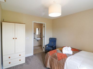A bedroom with a bed with folded towels a blue armchair a wardrobe and an open door leading to a bathroom at Teach Ards Kilgarvan County Kerry