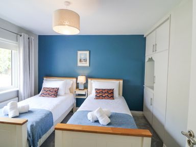 A bedroom with two single beds blue wall behind beds and a window with curtains at Teach Ards in Kilgarvan County Kerry