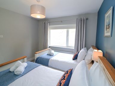 A bedroom with two single beds with blue throws and rolled towels under a window with curtains at Teach Ards Kilgarvan County Kerry