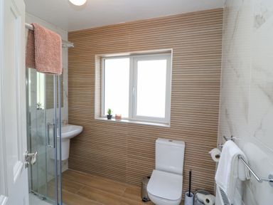 A bathroom with a glass shower enclosure a white sink a toilet a window with a small plant and candle on the sill at Teach Ards in Kilgarvan County Kerry