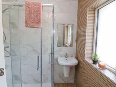 A bathroom with a glass shower cubicle a pedestal sink a mirror a window with a plant and candle at Teach Ards Kilgarvan County Kerry