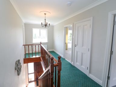 A hallway with green carpet and wooden handrail with doors leading to other rooms at Teach Ards in Kilgarvan County Kerry