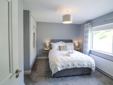A bedroom with a double bed bedside tables with lamps built in wardrobes and a large window at Teach Ards in Kilgarvan County Kerry
