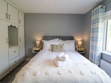 A bedroom with a double bed two bedside tables with lamps a built in wardrobe and a window with striped curtains at Teach Ards in Kilgarvan County Kerry
