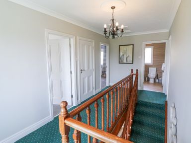 A hallway with green carpet and wooden banister with doors leading to rooms at Teach Ards Kilgarvan County Kerry