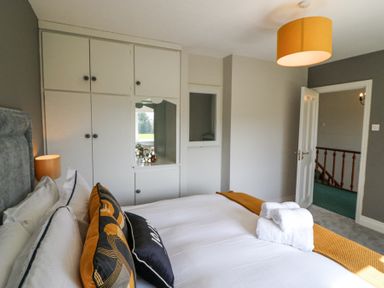 A bedroom with a bed with white linens and yellow and black pillows towels on the bed built in white cupboards and a yellow ceiling light at Teach Ards Kilgarvan County Kerry