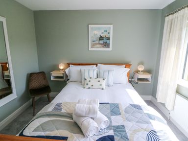 A bedroom with a bed with pillows towels and patterned quilt a chair mirror and bedside shelves with lamps at Teach Ards Kilgarvan County Kerry