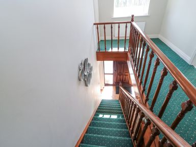 A staircase with green carpet and wooden railing leading to a wooden front door at Teach Ards in Kilgarvan County Kerry