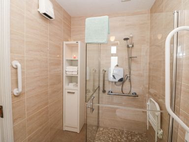 A bathroom with tiled walls a shower area a glass door white shelving unit with towels and a green towel hanging at Teach Ards Kilgarvan County Kerry