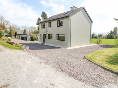 A two-story house with gravel driveway and green lawn surrounded by trees at Teach Ards Kilgarvan County Kerry