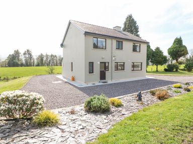 A two-story house with multiple windows surrounded by gravel driveway and landscaped garden at Teach Ards Kilgarvan County Kerry
