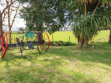 An old farming rake with red wheels on grass near trees and a wire fence in a rural field at Teach Ards in Kilgarvan County Kerry