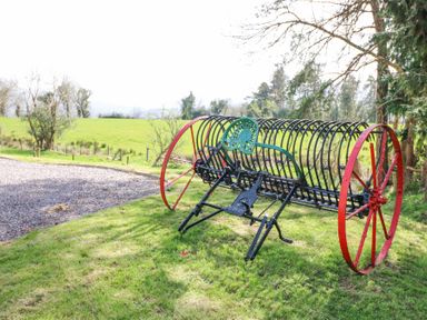 An old farming machine with red wheels and a green seat on grass near a gravel path and trees at Teach Ards in Kilgarvan County Kerry