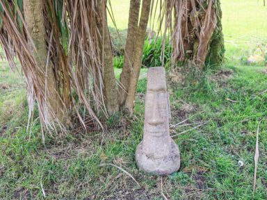A stone statue resembling a moai head on grass near tree trunks at Teach Ards in Kilgarvan County Kerry