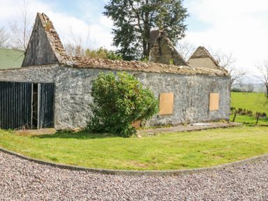 An old stone building with partially collapsed roof and boarded windows on a grassy area at Teach Ards in Kilgarvan County Kerry