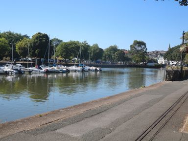 A river with moored boats and trees along the bank with buildings in the background at Joymead in Malborough