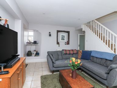A living room with gray sectional sofa a wooden coffee table with flowers a television on a wooden stand and stairs at Joymead in Malborough
