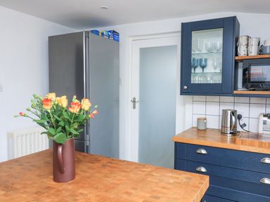 A kitchen with a wooden countertop a vase with flowers a silver refrigerator blue cabinets with glassware a kettle and a toaster at Joymead in Malborough