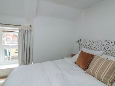 A bedroom with a white bed and decorative headboard two pillows and a curtained window at Joymead in Malborough