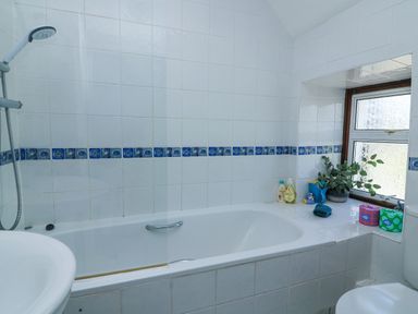 A bathroom with a bathtub shower combination a window with plants and toiletries at Joymead in Malborough