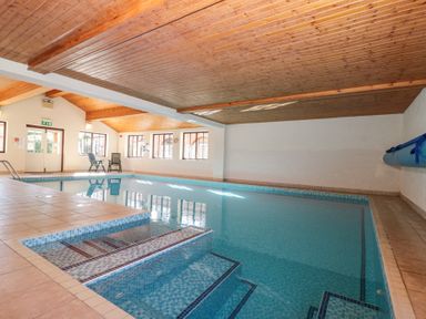 An indoor swimming pool with steps leading into the water and two chairs near windows at Beaver Cottage in Little Thirkleby near Thirsk