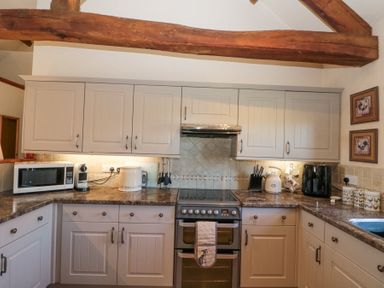 A kitchen with white cabinets a stove a microwave coffee machine and kitchen utensils at Beaver Cottage in Little Thirkleby near Thirsk