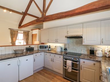 A kitchen with wooden beams white cabinets appliances and a window with curtains at Beaver Cottage in Little Thirkleby near Thirsk