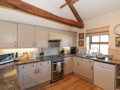 A kitchen with cabinets a stove a microwave dishwasher and a window at Beaver Cottage in Little Thirkleby near Thirsk