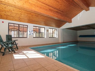 An indoor swimming pool with tiled floor three chairs and wooden ceiling at Beaver Cottage in Little Thirkleby near Thirsk