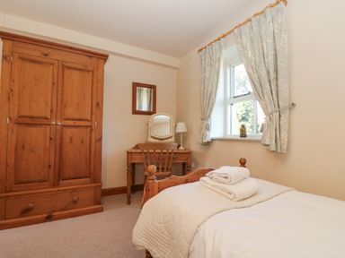 A bedroom with a wooden wardrobe a wooden desk and chair a bed with folded towels and a window with curtains at Beaver Cottage in Little Thirkleby near Thirsk
