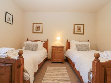 A bedroom with two single beds made with white bedding a wooden bedside table with a lamp and framed pictures on walls at Beaver Cottage in Little Thirkleby near Thirsk