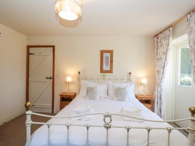 A bedroom with a white metal bed frame two bedside tables with lamps and floral curtains at Beaver Cottage in Little Thirkleby near Thirsk