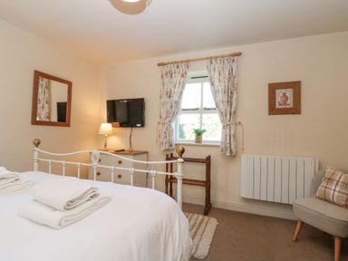 A bedroom with a white bed and towels on it a wall mounted television a window with floral curtains and a small plant on the sill at Beaver Cottage in Little Thirkleby near Thirsk