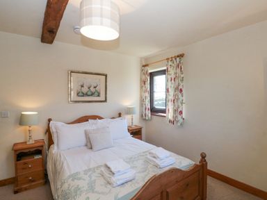 A bedroom with a wooden bed two bedside tables and floral curtains at Beaver Cottage in Little Thirkleby near Thirsk
