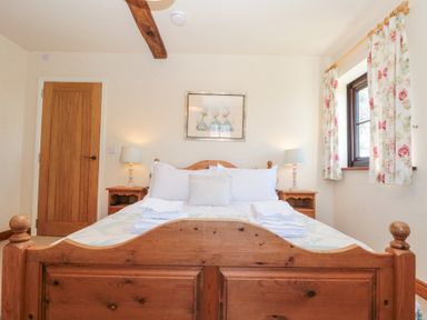 A bedroom with a wooden bed with white bedding two bedside tables with lamps a window with floral curtains and a wooden door at Beaver Cottage in Little Thirkleby near Thirsk
