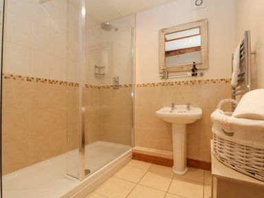 A bathroom with a walk in shower a pedestal sink a mirror and a wicker basket at Beaver Cottage in Little Thirkleby near Thirsk