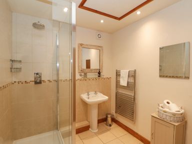 A bathroom with a shower area sink heated towel rail and a cabinet with toilet paper at Beaver Cottage in Little Thirkleby near Thirsk